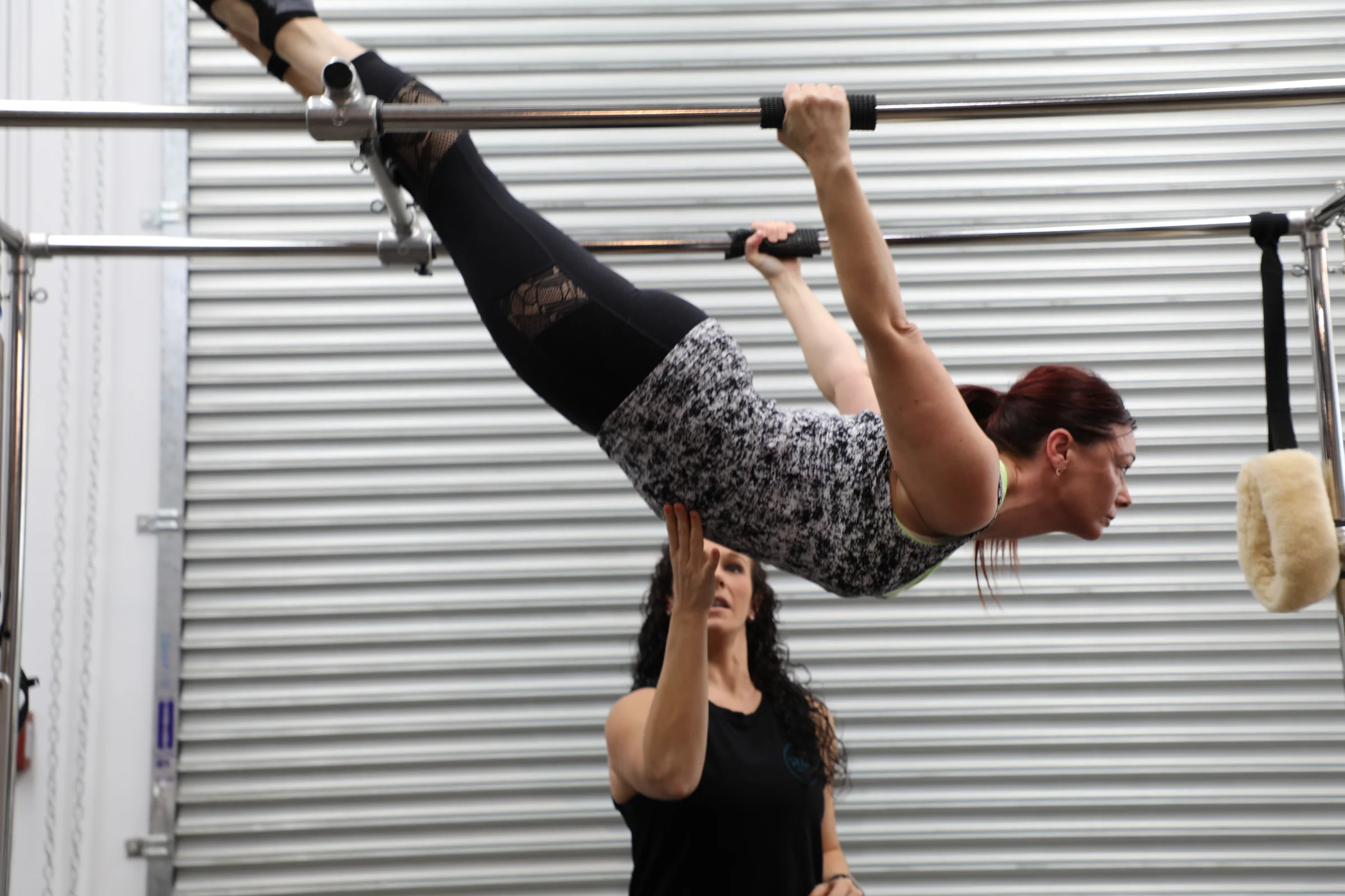 Client hanging from the trapeze table bar while an instructor spots