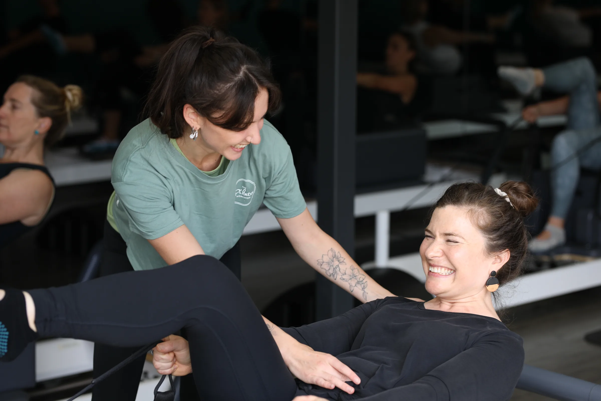 Pilates instructor giving hands-on cues to a smiling client on the reformer